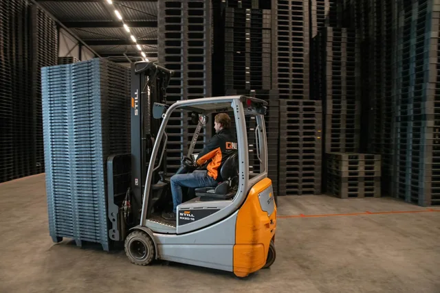 Heftruck tussen hoge stapels kunststof pallets in het magazijn van Q-Pall
